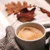 A picture of a cup of coffee with a book and some leaves in the background.