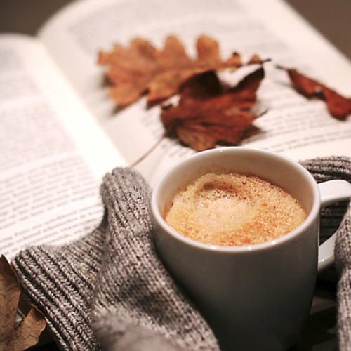 A picture of a cup of coffee with a book and some leaves in the background.